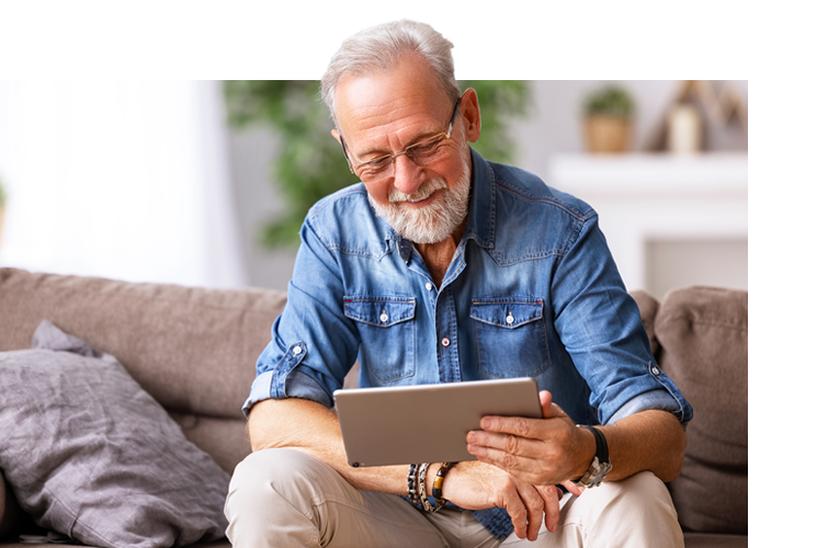 Ein &auml;lterer Mann sitzt gem&uuml;tlich im Sessel, l&auml;chelt und h&auml;lt sein Smartphone in der Hand.